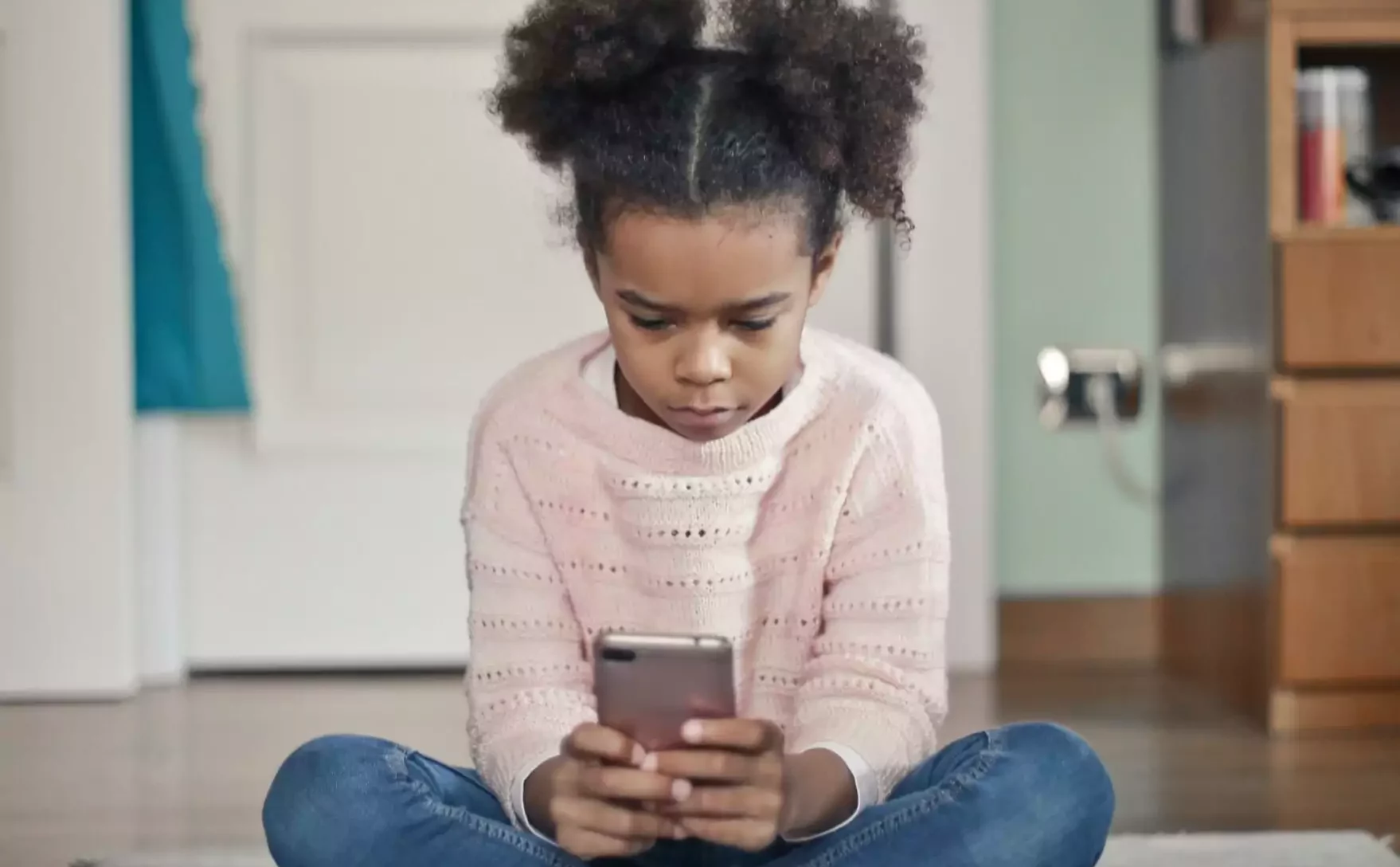 Petite fille assisse parterre à l'indienne avec smarphone